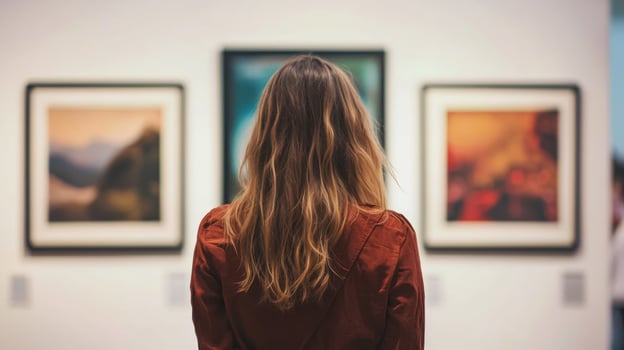 A woman with long hair standing in front of a wall with three framed paintings. photo