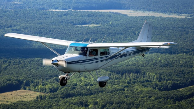 A small white airplane flying over a forested landscape with a clear blue sky. photo