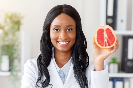 Positive black nutrition expert holding grapefruit at desk in medical office. Portrait of African American female dietitian with fresh fruit looking at camera and smiling in clinic photo