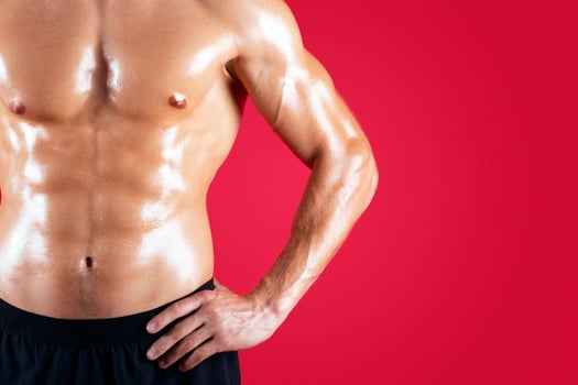 Closeup of sexy young guy with naked torso posing with hands on hips on red studio background, copy space. Cropped view of handsome fit man with six pack abs. Healthy living concept photo