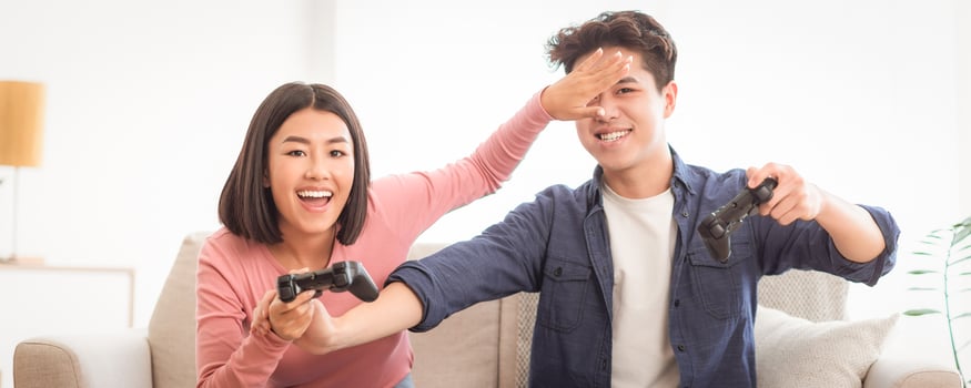 Joyful Japanese Couple Playing Game Having Fun Together Sitting On Sofa At Home. Family Weekend Leisure, Videogames And Computer Gaming Hobby Concept. Panorama photo