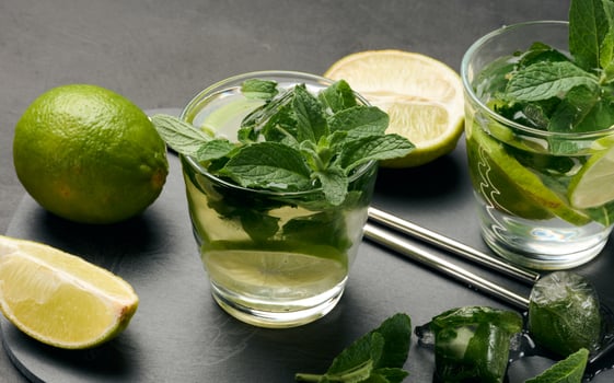 Glass of mojito cocktail with fresh mint leaves, lime slices, and ice cubes on a dark stone background. Refreshing summer drink with stainless steel straws photo