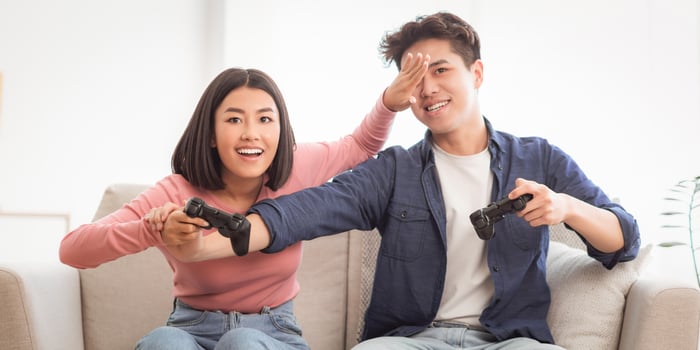 Cheerful Asian Spouses Having Fun Playing Game Together Sitting On Sofa Indoors. Chinese Girlfriend And Boyfriend Play Videogames At Home On Weekend. Computer Gaming Concept photo