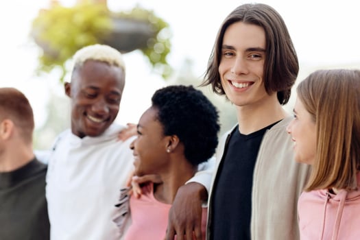 Cheerful handsome guy spending time with his international friends men and women, walking by street and embracing, having conversation, smiling and laughing, panorama. Millennials lifestyle photo