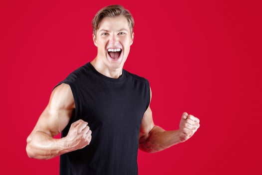 Emotional Caucasian sportsman screaming, making YES gesture, celebrating his victory on red studio background. Triumphant young bodybuilder winning competition, taking first place in sports contest photo
