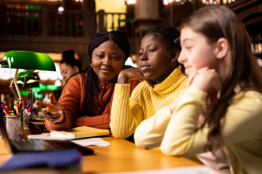 African american professor mentoring her teen girls students with an assessment, teaching academic concepts and enhancing their knowledge through practical exercises. Private lessons at the library. photo