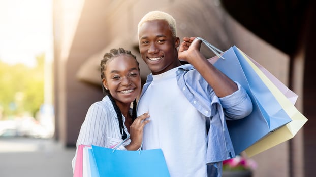 Closing of season and shopping. Smiling african american millennial man and woman with shopping bags hugs and looks at camera, near store, copy space photo