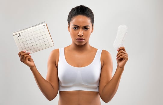 Angry unhappy young black woman demonstrates periods calendar and sanitary napkin, isolated on grey studio background. Women healthcare, menstruation, menstrual cycle, period delay concept photo
