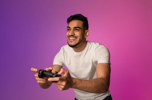 Happy young Arab guy with joystick playing game in neon light. Millennial middle Eastern gamer with controller participating in online gaming championship. Modern hobbies concept photo