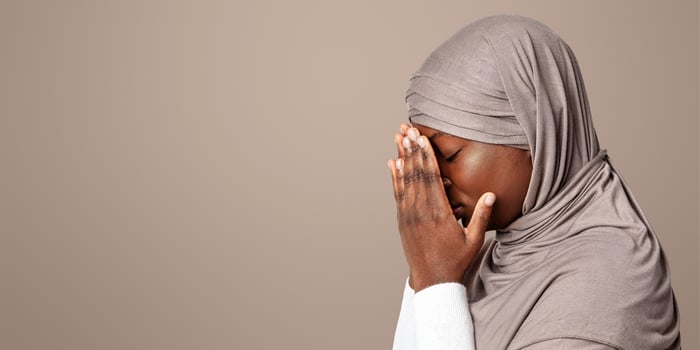 Upset black islamic lady in hijab covering face with hands, depressed african muslim woman in headscarf standing over light background, feeling ashamed, profile portrait with copy space photo
