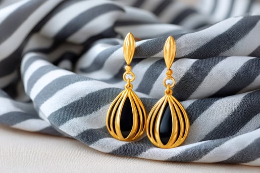 Pair of gold earrings with black onyx and diamonds resting on striped silk cloth photo