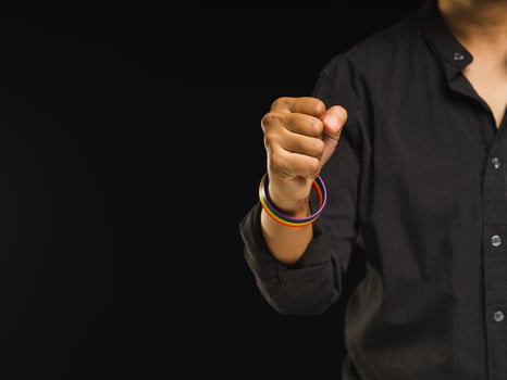 Hand fist with rainbow wristbands in a hand while standing against a black background photo