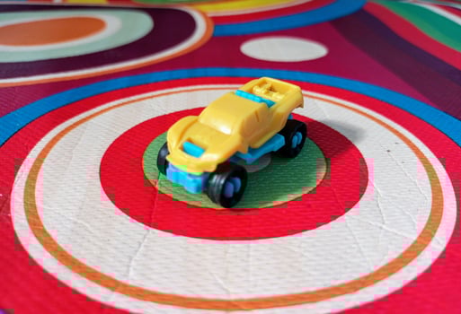 A Small Yellow and Blue Toy Car on a Colorful Circular Patterned Mat. photo