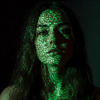 An adult female's face is covered in a pattern of green light dots in a dark setting photo