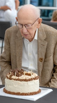 An old man sitting at a table with a cake photo