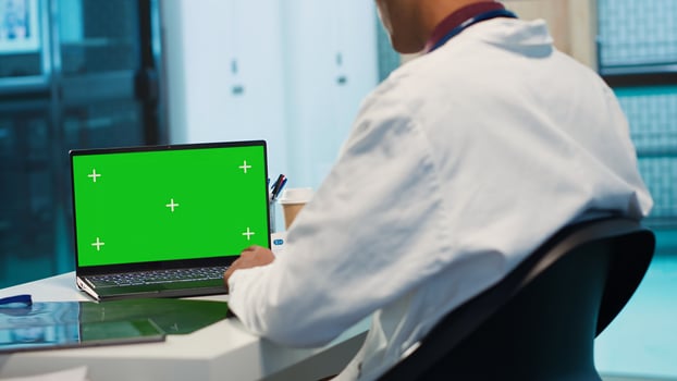 Indian physician works in his facility office next to chroma key, using modern technology for scan interpretation and results. Specialist offers professional advice based on records. Camera A. photo