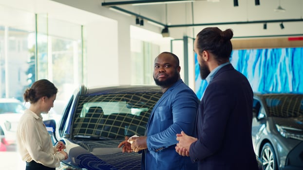 Clients arriving in car dealership, being greeted by friendly car salesman ready to showcase available vehicles to clients. Customers walking in showroom, being welcomed by agent, camera A photo