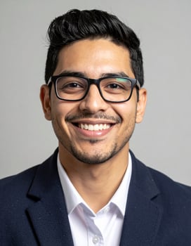 A young man with glasses smiles broadly in a business suit photo
