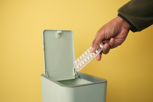 Disposing of medication in a green trash bin against yellow background photo