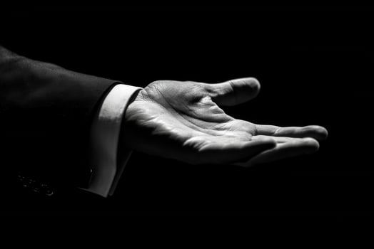 Elegant hand gesture in a formal suit, symbolizing invitation or offering against a dark backdrop photo