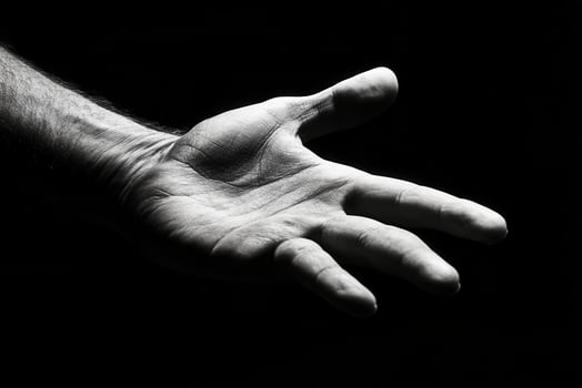 A close-up of a human hand reaching out against a black background, symbolizing connection photo