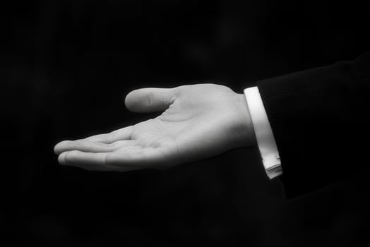A formal hand gesture inviting assistance, set against a blurred dark background photo