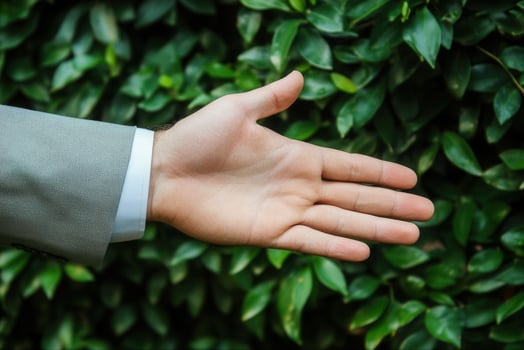 A business professional extending a hand for a handshake amidst lush green foliage photo