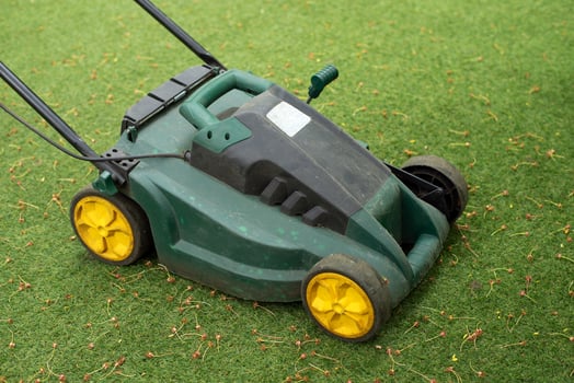 Old green lawn mower on artificial grass, close-up of used garden equipment with yellow wheels. photo