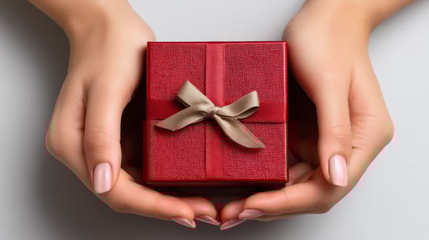Hands gently cradle a small open red box, unveiling a beautiful gift adorned with a ribbon. This moment captures the excitement of giving and receiving surprises. photo