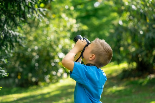 Cute boy in a blue T-shirt takes pictures with the camera in the park photo