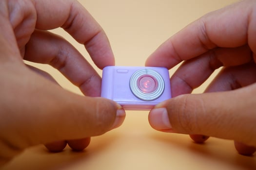 Hand Holding a Small Purple Toy Camera on Beige Background photo