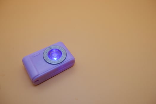 Purple Toy Camera with Glowing Lens on Beige Background photo