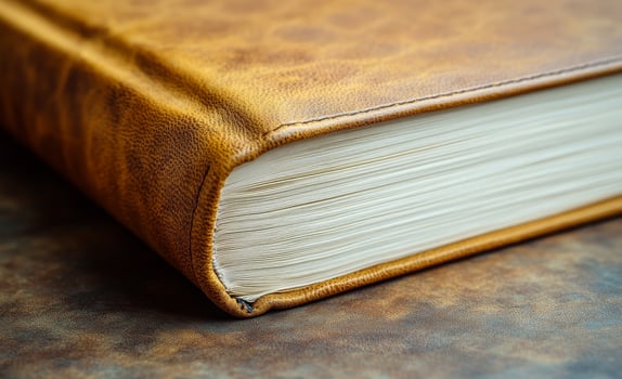 Leather-bound book on table. A leather-bound book with golden pages lays on a rustic table, showcasing its elegant cover and texture. photo
