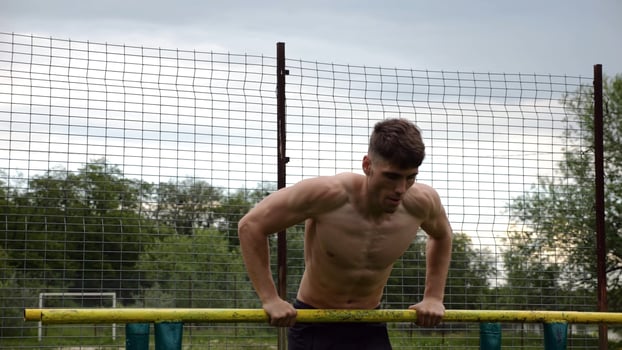 Male shirtless athlete doing push ups on parallel bars at natur. Strong sporty man exercising at sports ground. Young sportsman training hard outdoor. Concept of active sportive lifestyle. Slow mo photo