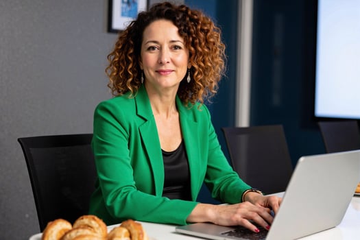 A woman in a green jacket sitting at a table with a laptop photo