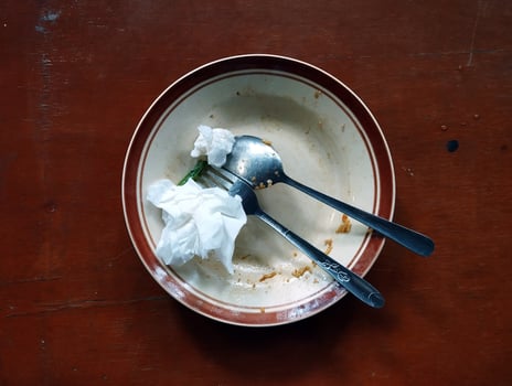 An empty plate with leftover food, a spoon, a fork, and some used tissues placed on a brown table. photo