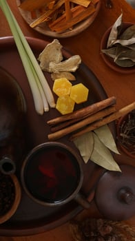 Top view of Wedang Uwuh on pottery tea cup with its composition that consist of sappan wood, cinnamon, ginger, lemongrass, and pala leaves, on pottery tray photo