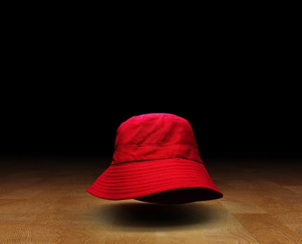 Red bucket hat on wooden floor, black background. photo
