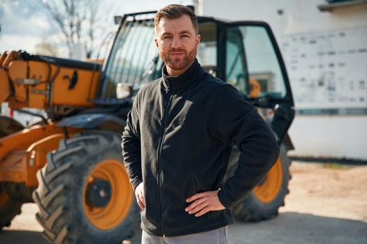 In black hoodie. Standing ,and posing. Man is with tractor. Agricultural worker photo