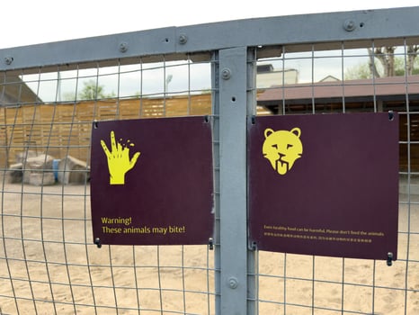 Warning signs on enclosure with dangerous animal in zoo. Inscription on sign about warning about biting animal. Concept of safety rules of visiting zoo. Do not feed the animals in cage, they can bite photo