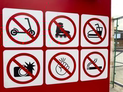 Closeup of red prohibition signboard with six warning icons indicating no scooters, rollerblades, bumper cars, flash photography, loud noises, or smoking in restricted area near entrance photo