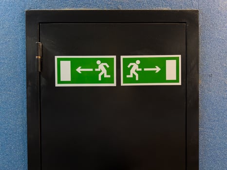 Two emergency exit signs with running figure and arrows pointing left and right placed on black door panel against blue wall, providing clear direction for safe evacuation in case of emergency photo
