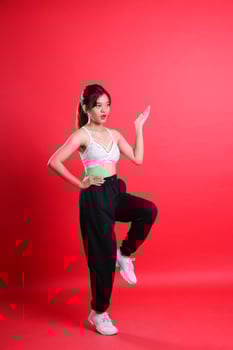 A woman in a sports bra and black pants raises one arm and leg in a studio, isolated on a red background photo