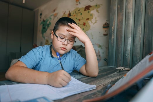 asian boy with glasses holding head in frustration, school task at home desk near world map wallpaper, concept of homeschooling, education service, tutoring support photo
