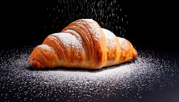 A freshly baked golden croissant dusted with powdered sugar, showcasing its flaky layers and buttery texture. photo