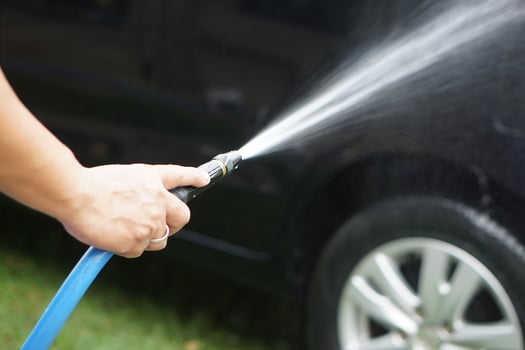 Close-up of a hand holding a gun pipe to spray high-pressure water onto a car during washing. This represents equipment used in car care, self-service washing, and regular car maintenance. photo