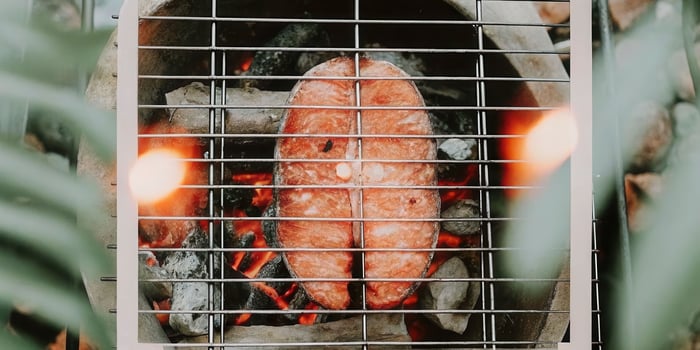 Grilled catfish steak closeup on metal grill grate surrounded by glowing coals and sizzling juices photo