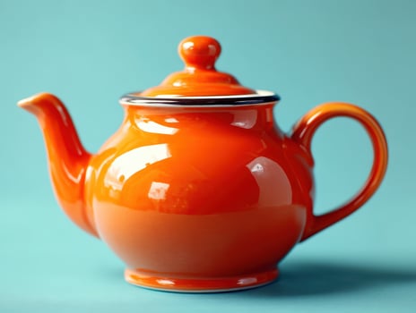 Bright orange teapot with a glossy finish, featuring a round body, a matching lid with a knob, curved spout, and elegant handle, set against a smooth turquoise backdrop photo