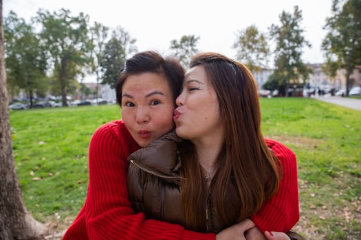 Two Chinese female friends hugging in the park. One kisses the other on the cheek photo