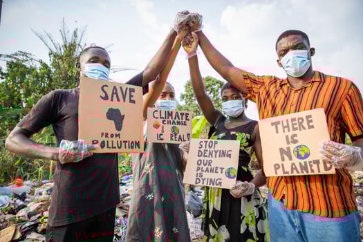 Four young adults protest with signs against pollution outside an illegal open landfill in Africa. photo